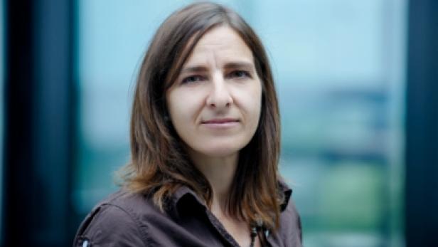 Eine Frau mit braunen Haaren und braunem Hemd blickt in die Kamera.