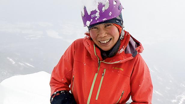 Eine lächelnde Frau mit Helm und roter Jacke im Schnee.