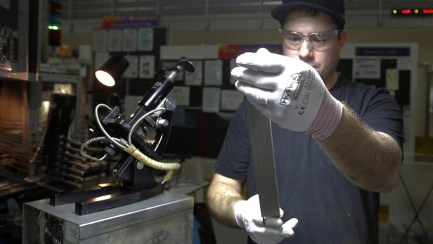 Ein Arbeiter mit Schutzbrille bearbeitet ein Metallstück mit einer Maschine.