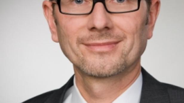 Ein Mann mit Brille, Anzug und Krawatte blickt in die Kamera.
