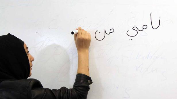 Eine Frau mit Hijab schreibt arabische Schriftzeichen auf eine weiße Tafel.