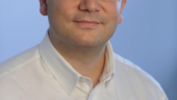 Ein Mann mit Brille und weißem Hemd vor einem blauen Hintergrund.