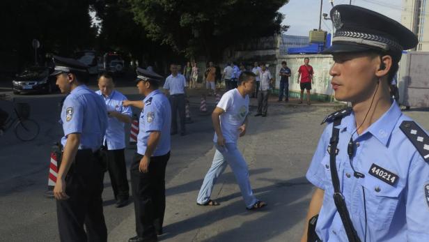 Chinesische Polizisten stehen auf einer Straße, während im Hintergrund eine Menschenmenge zu sehen ist.