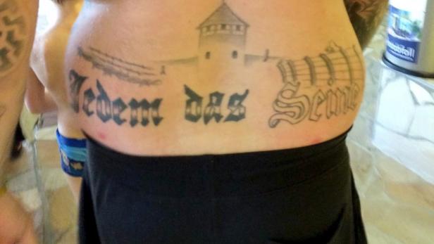 Eine Tätowierung auf dem Rücken einer Person zeigt ein Torhaus, Stacheldraht und den Schriftzug „Jedem das Seine“.