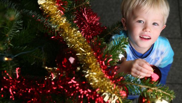 Ein kleiner Junge schmückt einen Weihnachtsbaum mit roten und goldenen Kugeln.