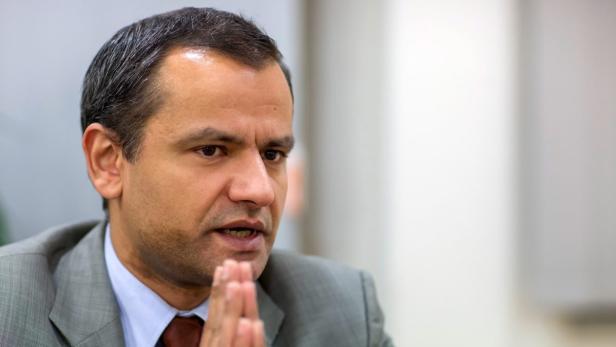 Ein Mann im Anzug spricht mit gefalteten Händen.