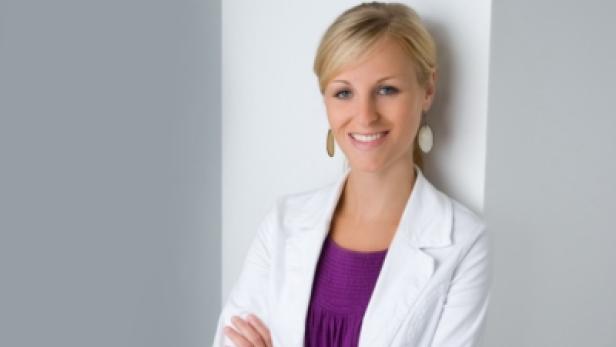 Eine blonde Frau mit verschränkten Armen lächelt in die Kamera.