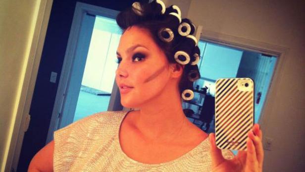 Eine Frau macht ein Selfie mit Lockenwicklern im Haar und Make-up im Gesicht.