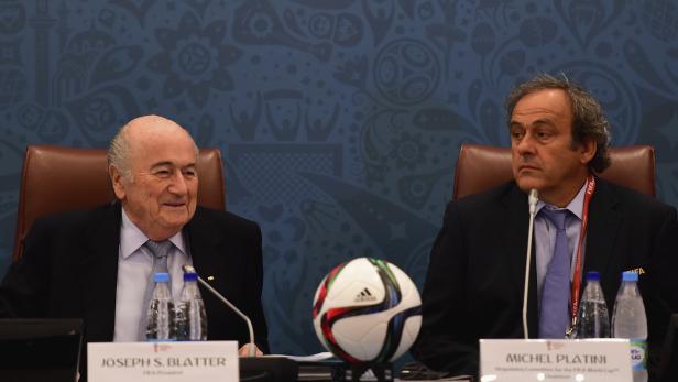 Joseph Blatter und Michel Platini sitzen an einem Tisch mit einem Fußball.