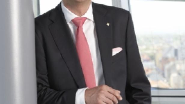 Ein Mann im Anzug mit Krawatte lehnt an einer Säule vor einem Fenster.