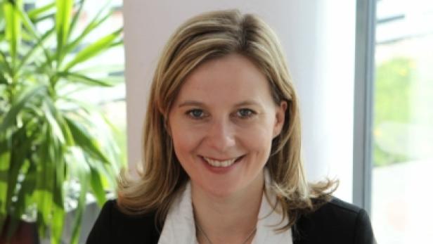 Eine lächelnde Frau mit blonden Haaren und einem schwarzen Blazer.