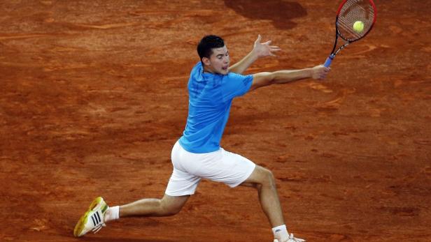 Ein Tennisspieler schlägt einen Ball auf einem Sandplatz.