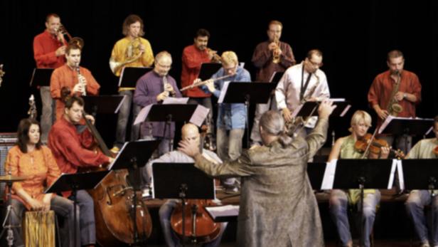 Ein Orchester spielt unter der Leitung eines Dirigenten auf einer Bühne.