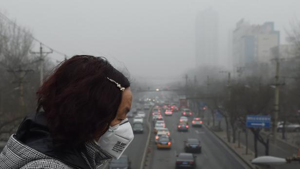 Eine Frau mit Atemschutzmaske blickt auf eine vernebelte Straße mit viel Verkehr.