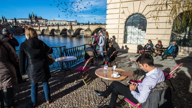 Menschen sitzen in einem Café in Prag mit Blick auf die Karlsbrücke.