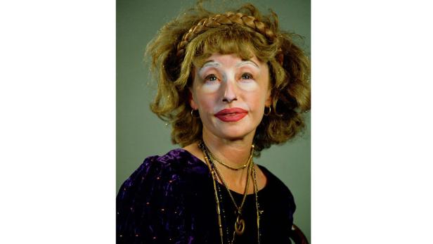 Eine Frau mit aufwendigem Make-up und goldenen Accessoires blickt in die Kamera.