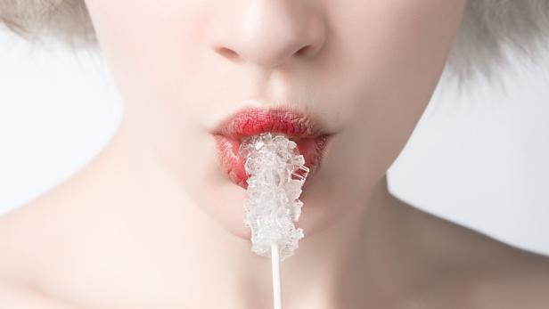Eine Frau hält einen Zuckerstängel zwischen ihren Lippen.