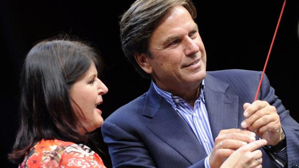 Ein Mann im Anzug hält einen roten Stab, neben ihm eine Frau mit floralem Oberteil.