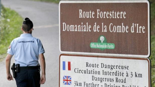 Ein Gendarm steht neben einem Schild, das auf eine gefährliche Waldstraße hinweist.