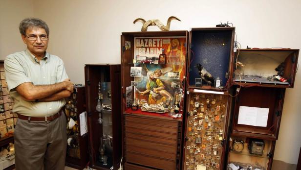 Ein Mann steht vor mehreren Schränken, die mit Sammlerstücken und einem Poster von „Hazreti Ibrahim“ gefüllt sind.