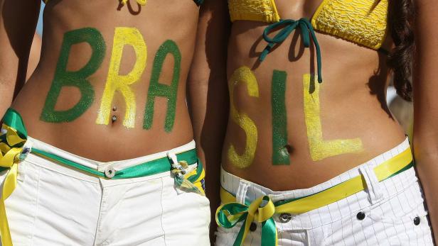 Zwei Frauen mit aufgemalten „Brasil“-Schriftzug auf dem Bauch, gekleidet in Bikinis und Shorts.