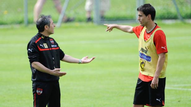 Ein Trainer gestikuliert mit einem Fußballspieler auf einem grünen Rasen.