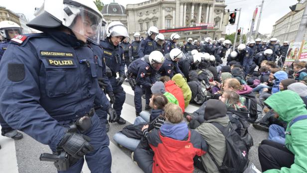 Polizisten in Wien räumen eine Sitzblockade von Demonstranten auf der Straße.