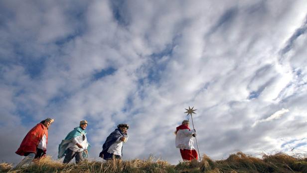 Sternsinger ziehen mit einem Stern vor bewölktem Himmel durch die Landschaft.