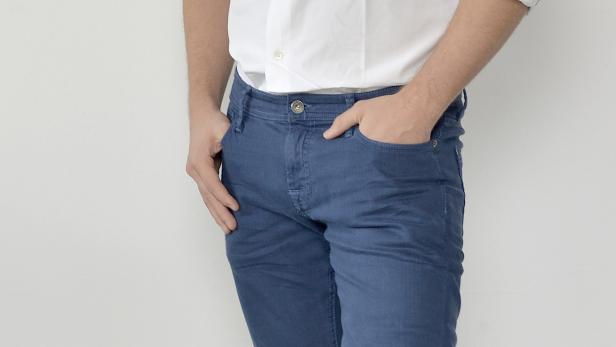 Ein Mann in Jeans, Hemd und Turnschuhen steht vor einer weißen Wand.