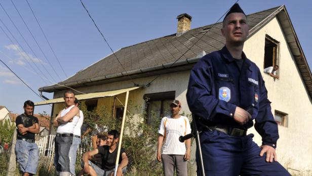 Ein Polizist steht vor einer Gruppe von Männern und einem Haus.