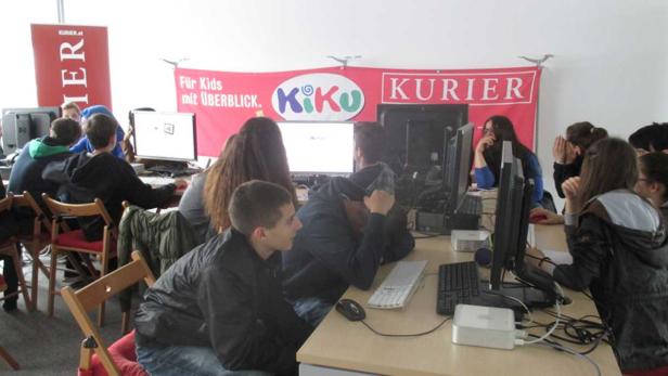 Eine Gruppe von Jugendlichen sitzt an Computern unter einem „Kiku“-Banner.