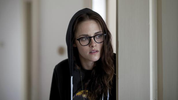 Kristen Stewart mit Brille und Kapuzenpullover steht an einer Tür.