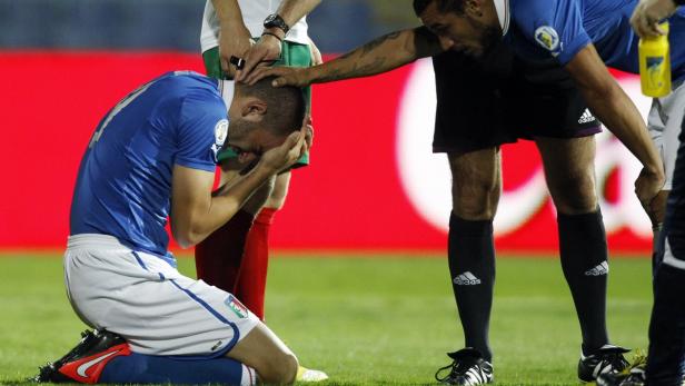 Ein Fußballspieler kniet verzweifelt auf dem Rasen, während andere ihn trösten.