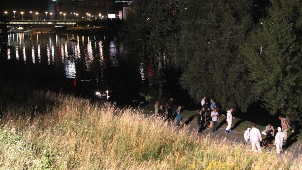 Am Ufer eines Flusses versammeln sich Menschen, während Spurensicherung in weißen Anzügen arbeitet.