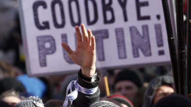 Eine Hand reckt sich vor einem Protestschild mit der Aufschrift „Goodbye, Putin!“.
