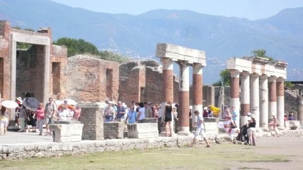 Besucher erkunden die Ruinen von Pompeji vor einer Bergkulisse.