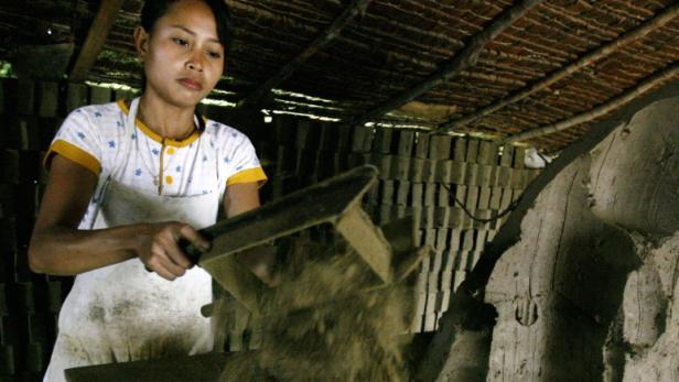 Eine Frau formt in einer Werkstatt Ziegelsteine aus Lehm.