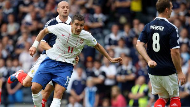 Ein Fußballspieler im weißen Trikot wird von einem Gegenspieler bedrängt.
