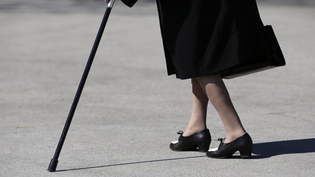 Eine Person mit einem Gehstock und schwarz-weißen Schuhen geht auf einer ebenen Fläche.