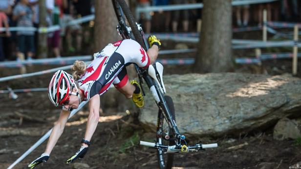 Eine Radfahrerin in kanadischer Sportbekleidung stürzt mit ihrem Mountainbike.