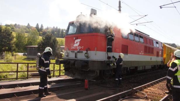 Feuerwehrleute löschen einen Brand in einer roten Lokomotive.