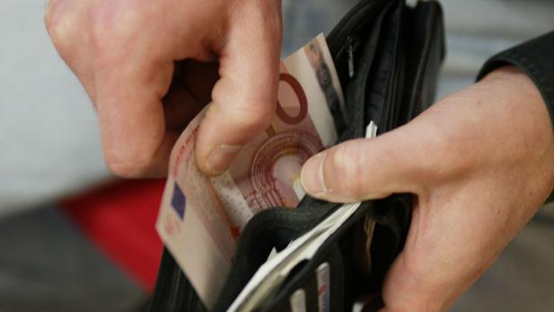 Eine Person nimmt einen 10-Euro-Schein aus einem schwarzen Portemonnaie.