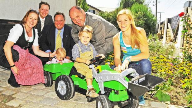Eine Gruppe von Erwachsenen und Kindern posiert mit einem grünen Spielzeugtraktor.