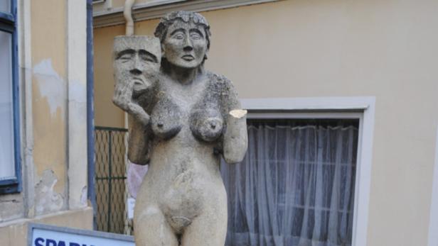 Eine Statue einer nackten Frau, die eine Maske in der Hand hält.