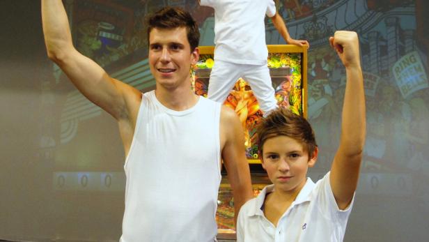 Ein Mann und ein Junge stehen mit erhobenen Fäusten vor einem Flipperautomaten.