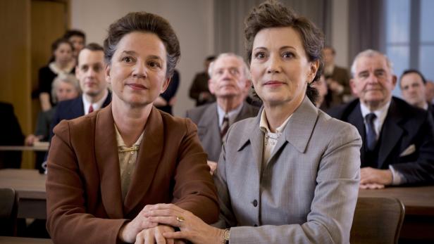 Zwei Frauen sitzen in einem Gerichtssaal, umgeben von anderen Zuhörern.