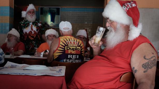 Eine Gruppe von als Weihnachtsmänner verkleideten Männern sitzt an einem Tisch und trinkt Bier.