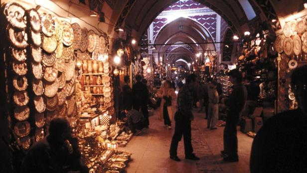 Menschen besuchen einen belebten Markt mit Waren, darunter Teller und Vasen.