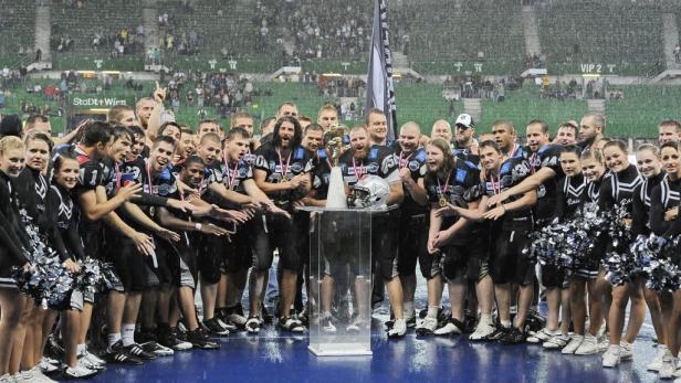 Ein American-Football-Team feiert mit Cheerleadern im Regen einen Pokalgewinn.