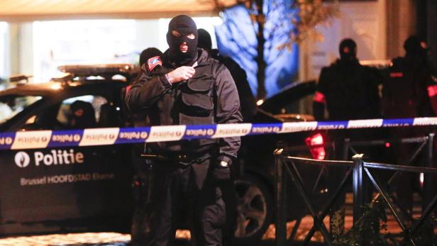 Ein Polizist mit Sturmhaube steht vor einem Polizeiauto in Brüssel.